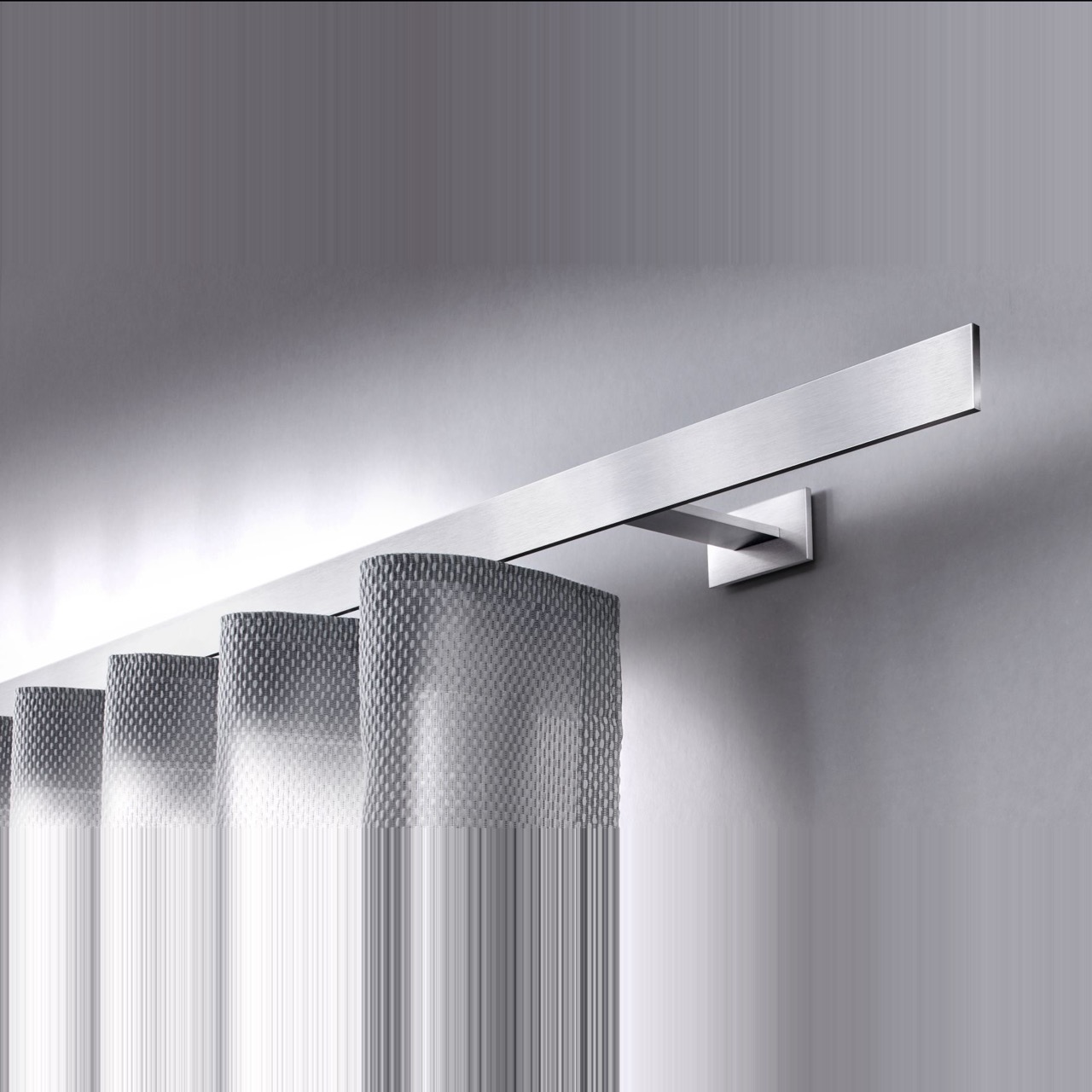 Nahaufnahme des Interstil Vorhangschienensystems „Codex“. Eine flache, minimalistische Vorhangschiene aus hochwertigem, matt gebürstetem Aluminium, die mit einem eckigen Wandhalter montiert ist. An der Schiene hängt ein heller Wellenvorhang mit einer dezenten Netzstruktur. Das Design wirkt modern und geradlinig.