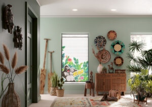 Gemütliches Interieur im afrikanischen Stil mit Wandtellern und Massivholz. Das mittige Fenster ist mit einem bedruckten Plissee dekoriert, das eine Urwaldszene und eine illustrierte Affenfigur im Comic-Stil darstellt.