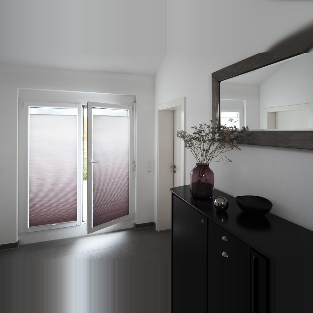 Nahaufnahme eines hellgrauen MHZ Wabenplissees an einem Fenster. Das Sonnenlicht scheint von hinten durch den Stoff, wodurch die charakteristische Wabenstruktur und das sanfte Lichtspiel im Material sichtbar werden. Das Plissee ist als Sichtschutz im unteren Fensterteil positioniert.