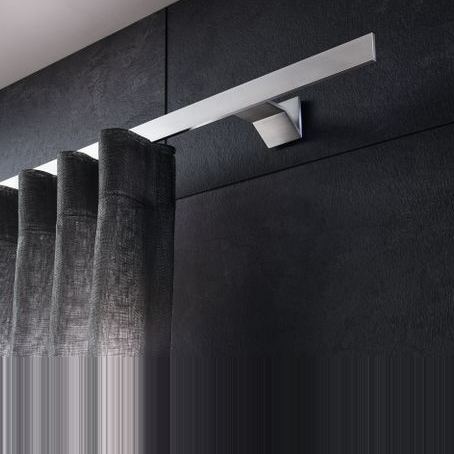 Nahaufnahme des Interstil Vorhangschienensystems „Index“. Eine flache, minimalistische Vorhangschiene aus hochwertigem, matt gebürstetem Aluminium, die mit einem eckigen Wandhalter montiert ist. An der Schiene hängt ein heller Wellenvorhang mit einer dezenten Netzstruktur. Das Design wirkt modern und geradlinig.