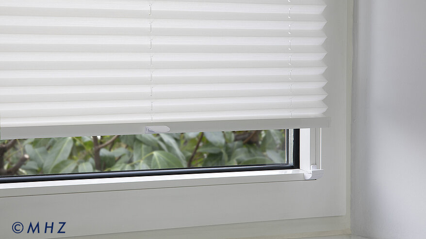 Detailansicht der Montage eines MHZ Plissees: Weißer Faltenstore befestigt mit einem unauffälligen Klemmhalter (Glasleistenträger) am Fensterrahmen.