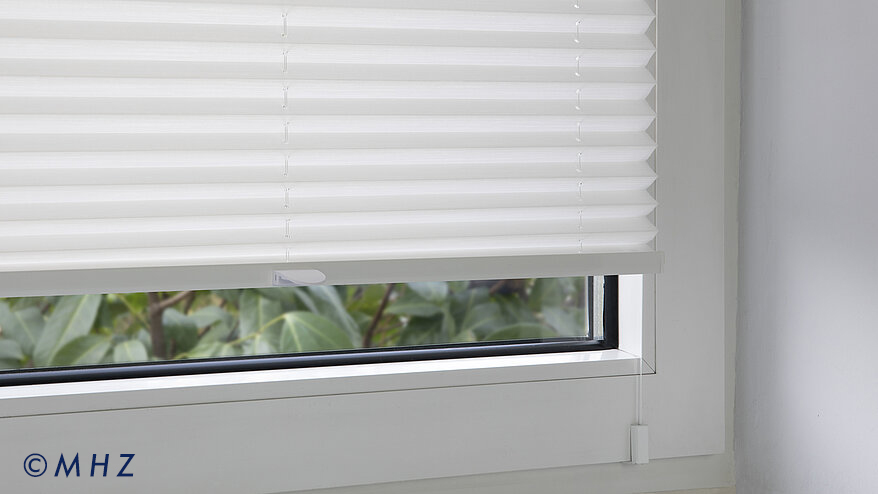 Montagebeispiel eines MHZ Plissees am Fensterrahmen: Ein weißer Fensterclip fixiert die Spannschur des Plissees sicher am Rahmenprofil, ideal für eine bohrfreie Montage
