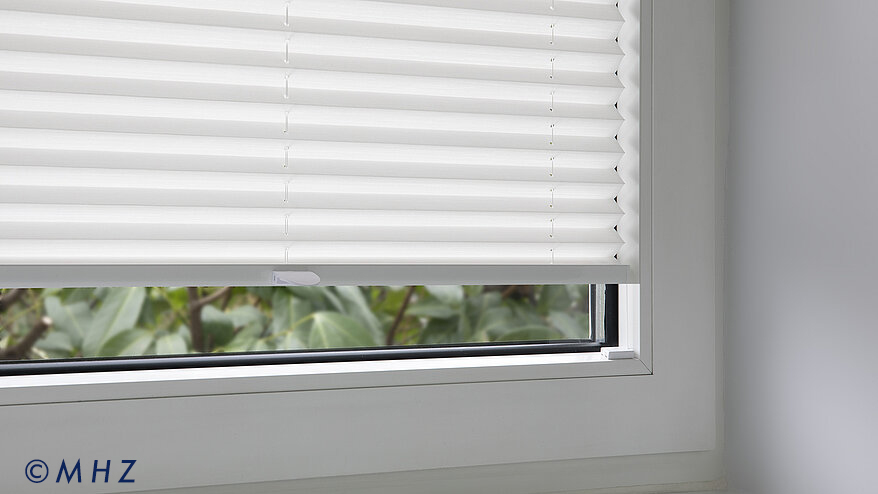 Detailansicht eines weißen MHZ Plissees, das mit einem Spannschuh direkt in der Glasleiste des Fensters montiert ist.