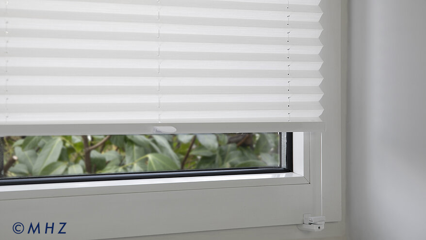 Montageart Klemmträger: Detailansicht eines weißen Plissees, das ohne Bohren durch eine Klemmvorrichtung sicher am Rahmen des Kunststofffensters fixiert ist.